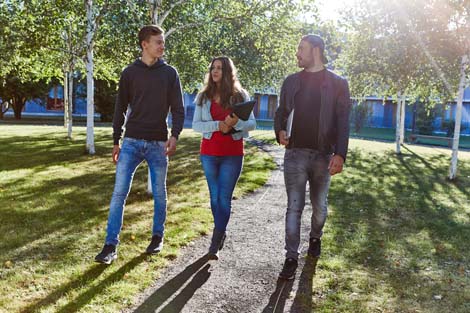 Auf dem Bild sind drei Studierende zu sehen wie sie über den Campus laufen.